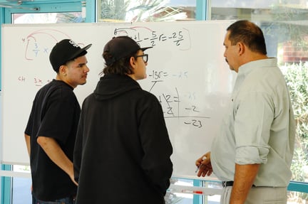 Students and teacher standing together looking a whiteboard with math equations