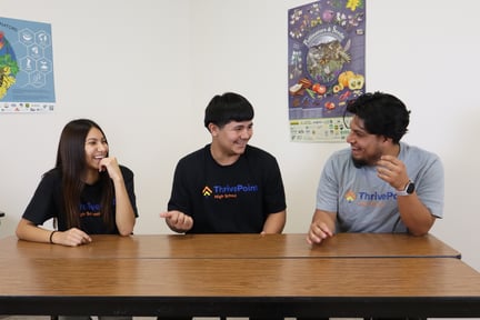 Three students sitting a desk talking and smiling