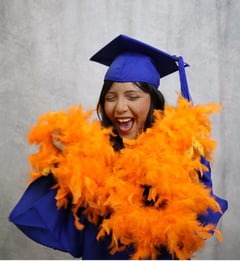 a graduating student in a blue cap and gown wearing orange feathers