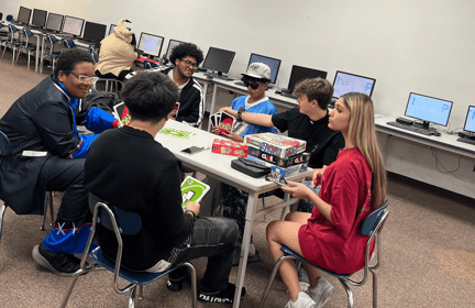 a group of teen students sitting at a table playing uno