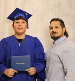 a student in a blue gown holding a diploma standing next to a student success coach