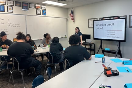 classroom of students sitting down at a table while learning about financial literacy