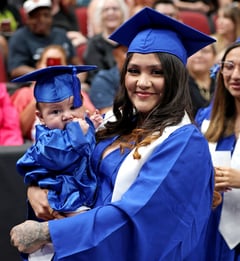 graduating student in a blue gown holding a baby