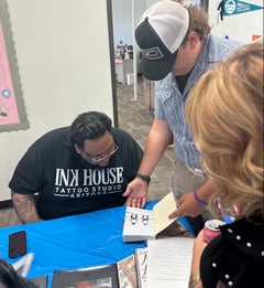student showing a tattoo artist a drawing in his notebook