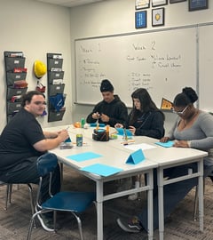students sitting at a table folding blue papers