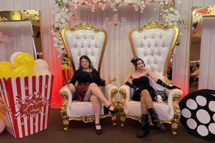 two students sitting on big white and gold chairs at prom